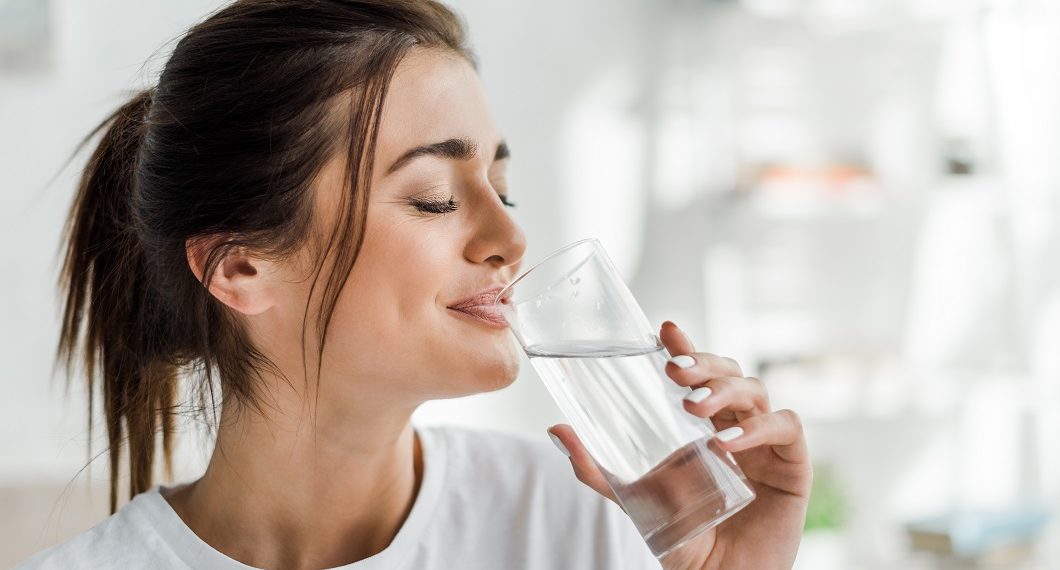 smiling girl holding drinking water from glass in the morning