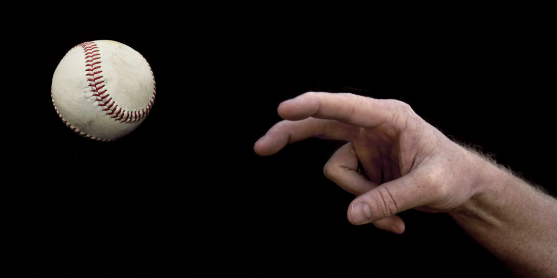 A manâ€™s arm throwing a baseball on a black background.