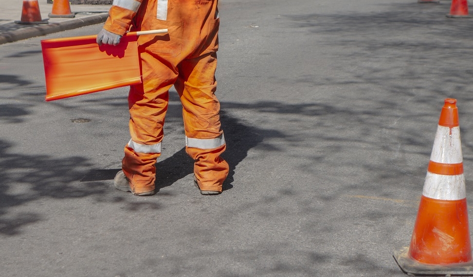 road worker directing traffic with orange flag and reflective suit