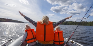Girl in a life jacket floating on the boat with his hands up. Children in life jackets sitting next