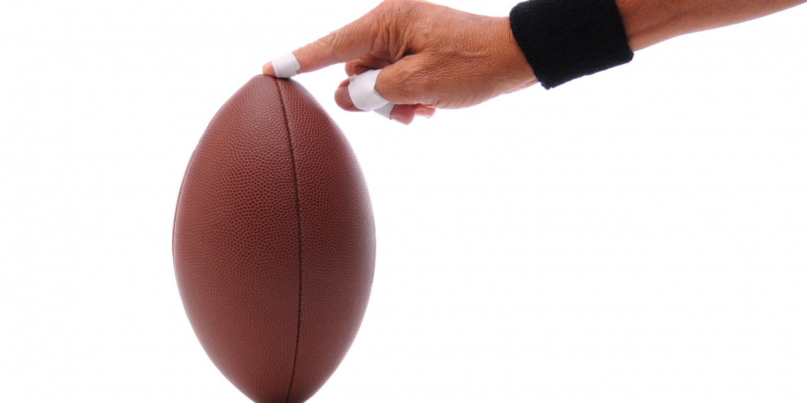 A man's hand holding an american football ready for place kicking. Horizontal format isolated on white with reflection.