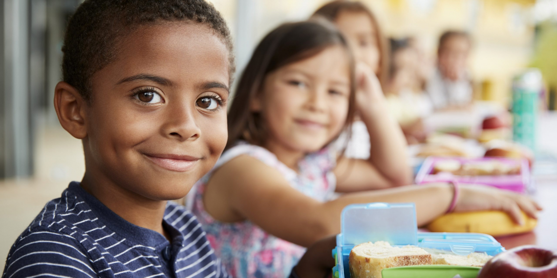 Young boy and girl at school lunch table smiling to camera