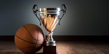 Basket ball and gold bright trophy on hardwood floor.