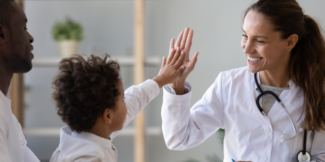 Smiling young female pediatrician give high five to little african American boy at consultation in clinic, happy woman doctor consult biracial toddler kid in hospital. Children healthcare concept